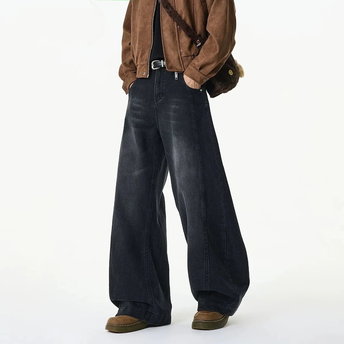 A person wearing dark wide-leg denim jeans, a brown suede jacket, and brown shoes, shown from the chest down against a plain white studio background.
