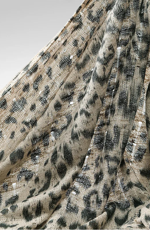 A close-up of a leopard print fabric with black and gray spots on a beige background, draped in soft folds.