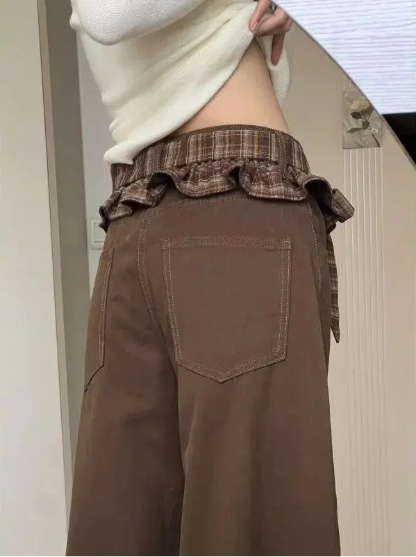 A person wearing brown wide-leg pants with a brown plaid ruffled waistband and a cream-colored knit top, shown from the back in an indoor setting.