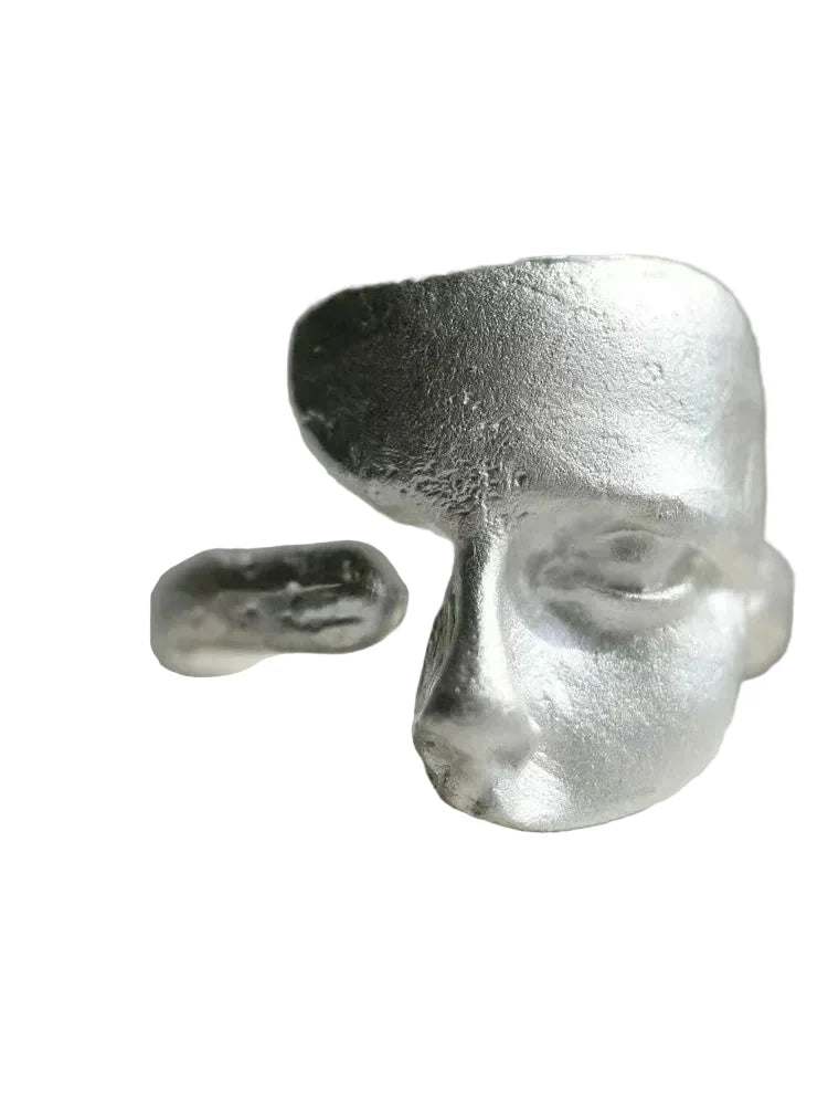 Silver ring with a face design on a gray background
