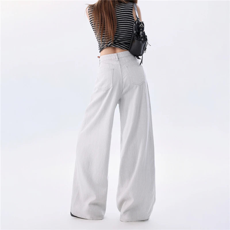 A model shown from the back wearing high-waisted, wide-leg white pants, a black and white striped crop top, and carrying a small black shoulder bag against a plain white studio background.