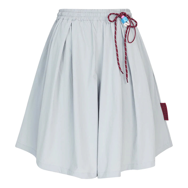 A light gray pleated shorts with an elastic waistband, a red patterned drawstring tied in a bow, and a small red brand tag on the side, shown against a plain white background.