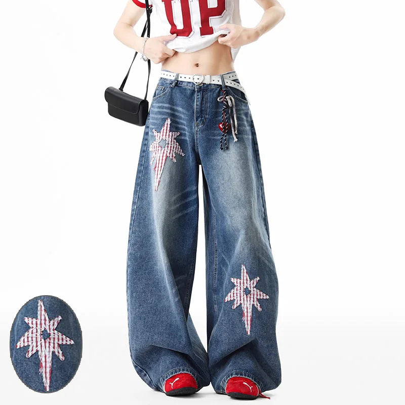 A model wears wide-leg blue denim jeans featuring large red-and-white star patches on the thighs and lower hems, styled with a white crop top, red shoes, and a black crossbody bag. A circular inset shows a close-up of one of the denim star patches.
