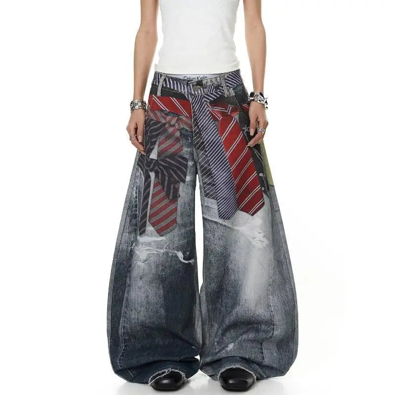 A model wearing extremely wide-leg, baggy denim pants with a printed pattern of various colorful neckties, paired with a white top and black shoes, shown from the waist down on a white background.