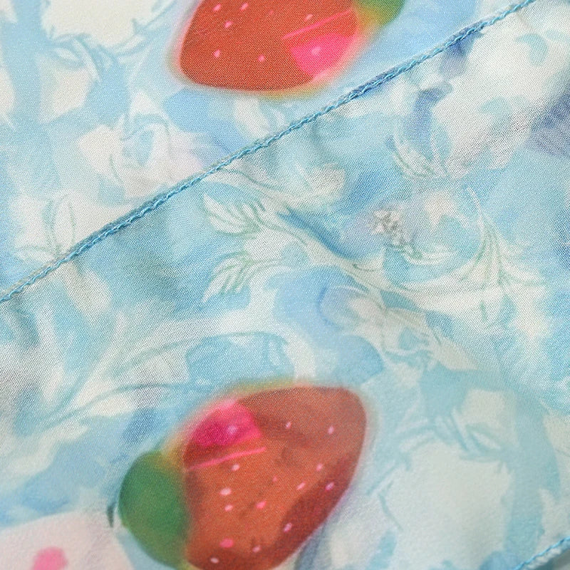 A close-up of a light blue patterned fabric with a white floral design and strawberry motifs, showing a diagonal seam.