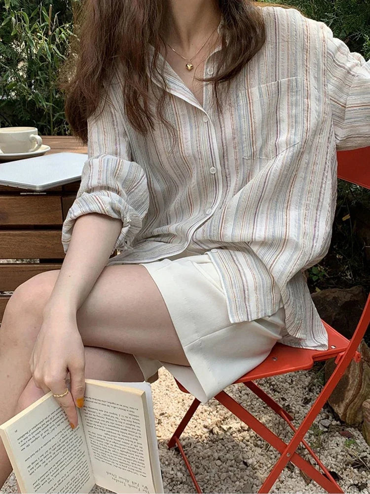 Woman sitting outdoors on a red chair, reading a book, wearing a striped shirt and shorts.