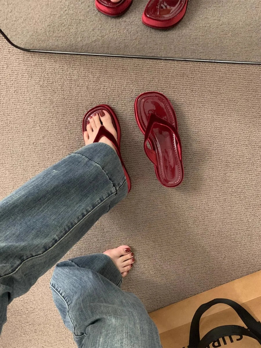 A person wearing blue jeans and a red thong sandal, with the second red thong sandal placed on the beige carpet beside them.