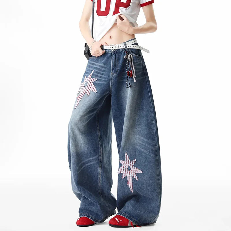 A person wearing very wide-leg blue denim jeans with red and white star embellishments on the legs, styled with a white crop top and red shoes against a plain white background.