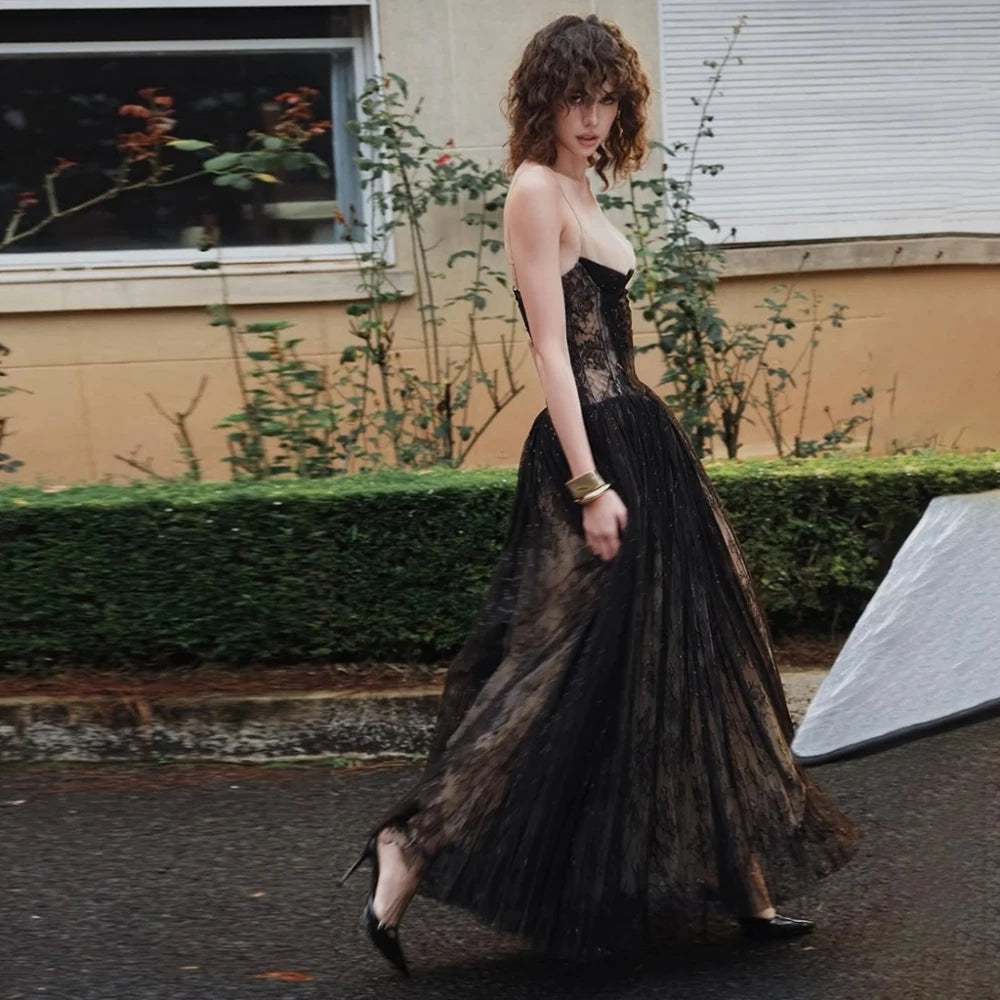 Woman in a black lace dress standing outdoors with a garden background