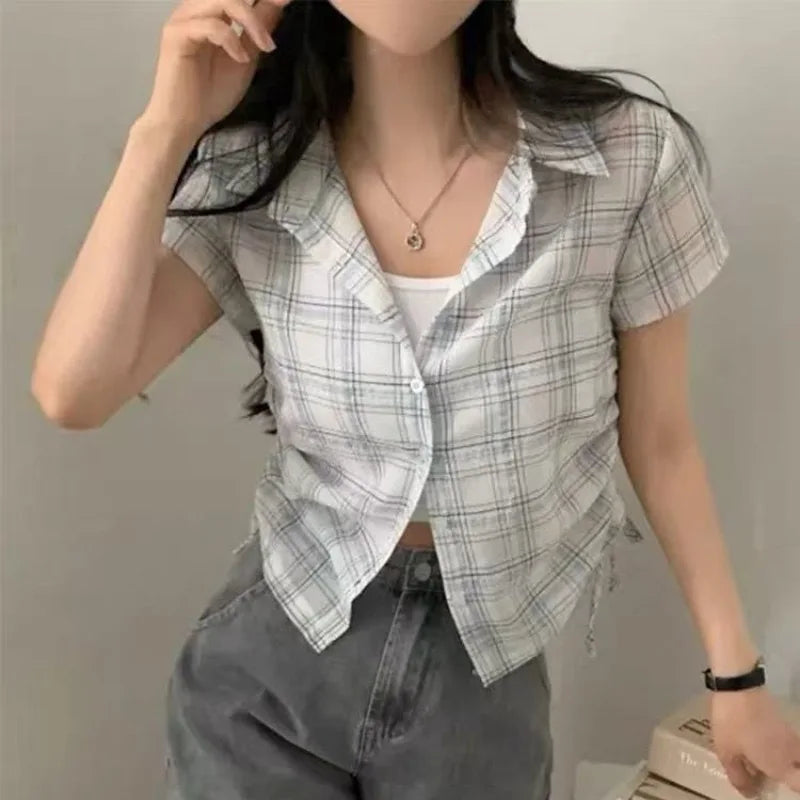 Person wearing a plaid shirt over a white top with gray pants against a plain background