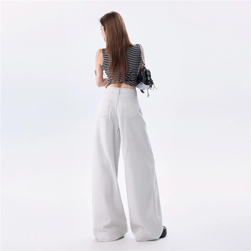 A woman shown from the back wearing a black and white striped sleeveless crop top, high-waisted white wide-leg pants, and carrying a small black shoulder bag against a plain white studio background.