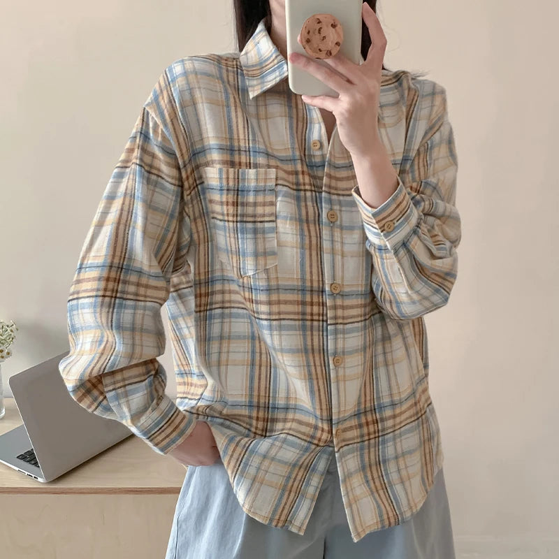 Person wearing a plaid shirt taking a mirror selfie in a room with a laptop on a desk.