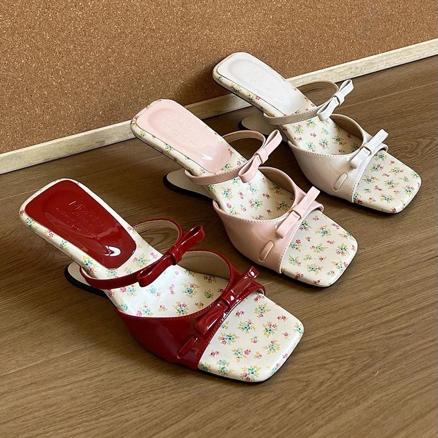 Pair of floral-patterned shoes with red soles on a wooden floor.