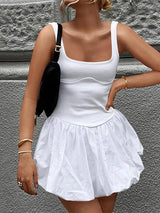 Person wearing a white tank top and skirt against a gray stone wall.