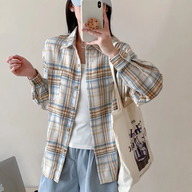Person wearing a plaid shirt holding a phone, with a plain background