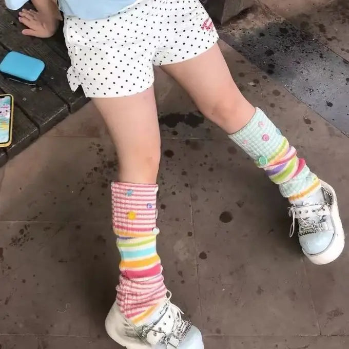 A person wearing white polka dot shorts and colorful striped knee-high socks with white sneakers, photographed in a real environment on a tiled floor.