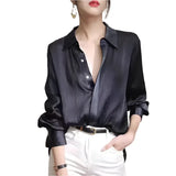 Person wearing a black satin shirt with white pants on a plain background