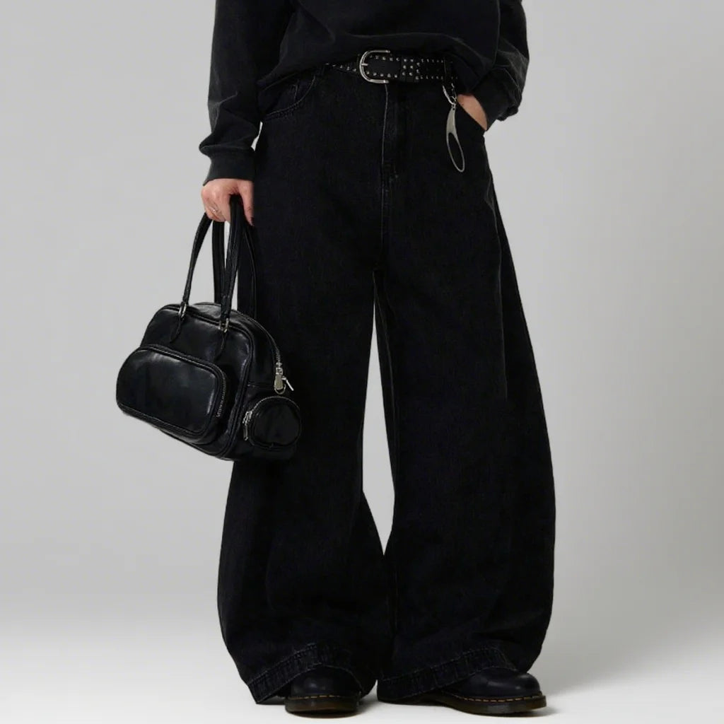Person wearing black wide-leg pants holding a black handbag against a plain background