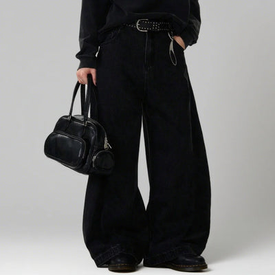 Person wearing black wide-leg pants holding a black handbag against a plain background