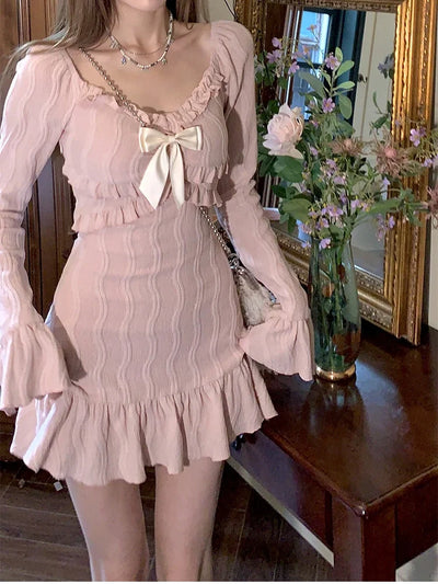 Person wearing a vintage-style dress with a bow detail in a room with flowers and a mirror.