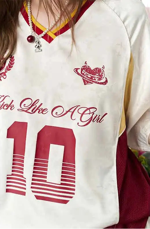 A close-up of a person wearing a white V-neck athletic-style top with red and yellow trim, red script text reading 'Rich Like A Girl,' a large red number 10 on the front, and a small red chest graphic.