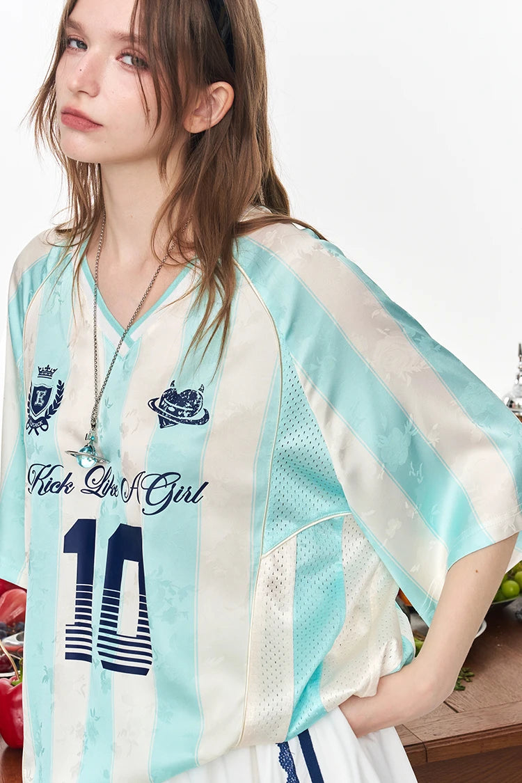 A woman wearing a light blue and white striped jersey top with 'Rich Girls Girl' and the number 10 printed on the front, styled with a silver necklace.