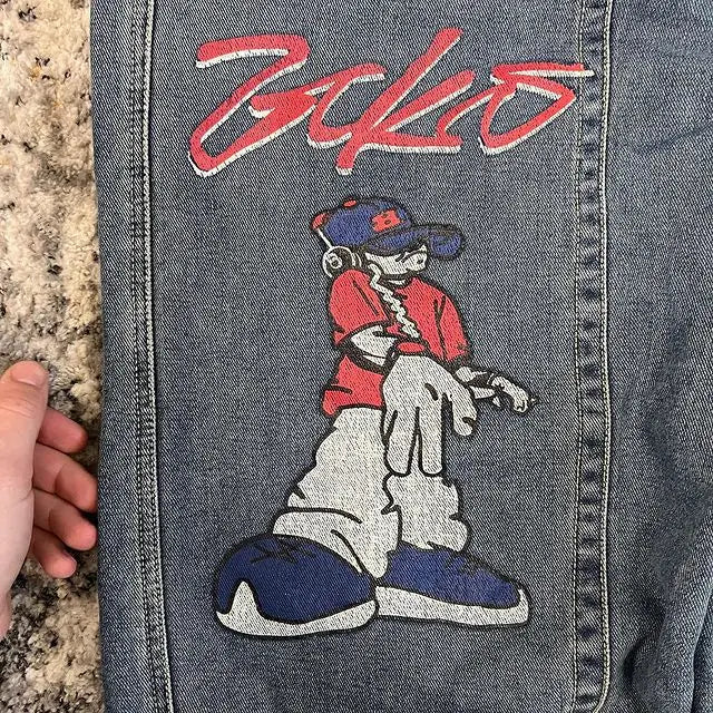 Close-up of a pair of blue denim jeans showing a large embroidered graphic on the back pocket. The embroidery features a cartoon character in a red shirt, white pants, and blue shoes, with the word 'Boko' in red script above it.