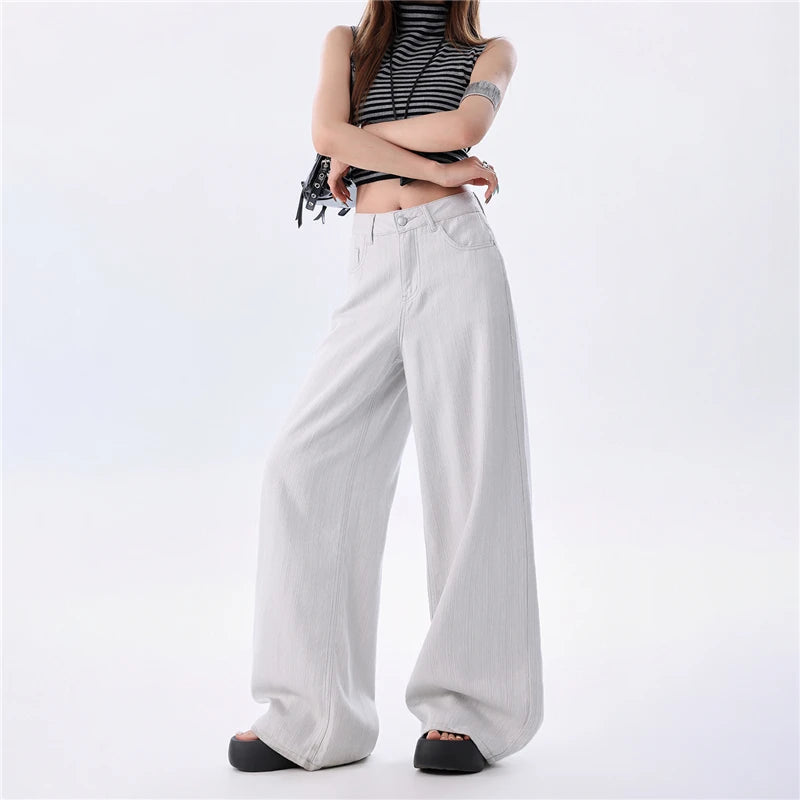 A model wearing light gray wide-leg pants, a black and white striped crop top, and black platform sandals, standing against a plain white studio background.