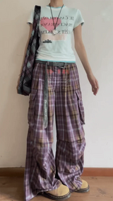 Person wearing a light-colored t-shirt with text and plaid pants against a plain background
