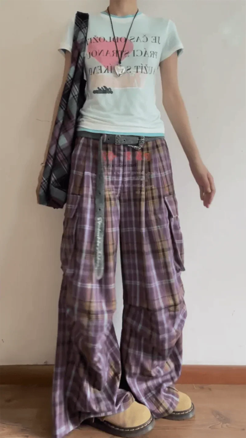 Person wearing a light-colored t-shirt with text and plaid pants against a plain background