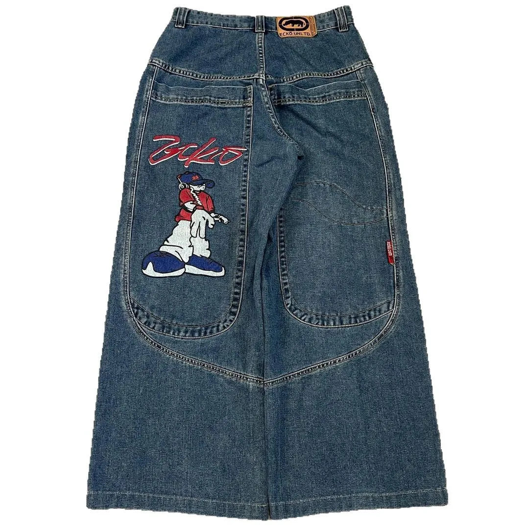 A pair of blue denim Jeans featuring a large embroidered cartoon dog patch on the left leg and a red script logo on the right thigh, shown against a plain white background.