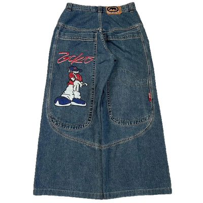 A pair of blue denim Jeans featuring a large embroidered cartoon dog patch on the left leg and a red script logo on the right thigh, shown against a plain white background.