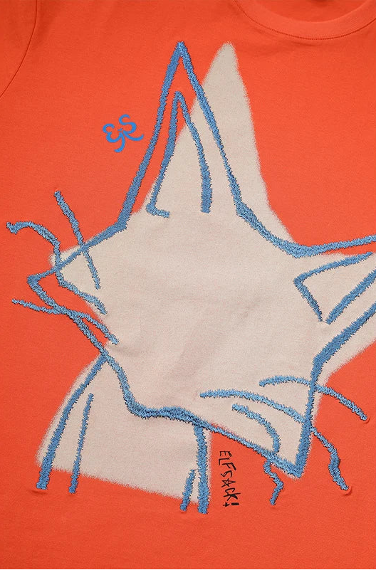 Close-up of a bright orange T-shirt featuring a large white star graphic outlined in blue, with a small blue monogram and the brand name 'ELFSKI' printed near the bottom of the star.