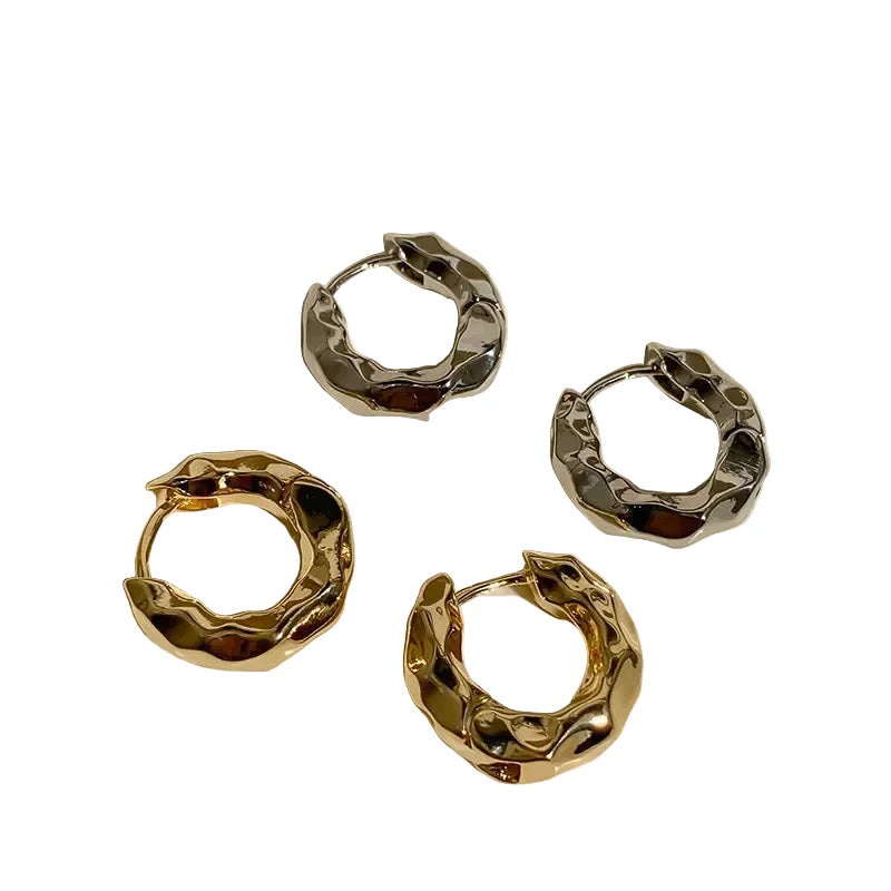 Four gold and silver hoop earrings on a light beige background
