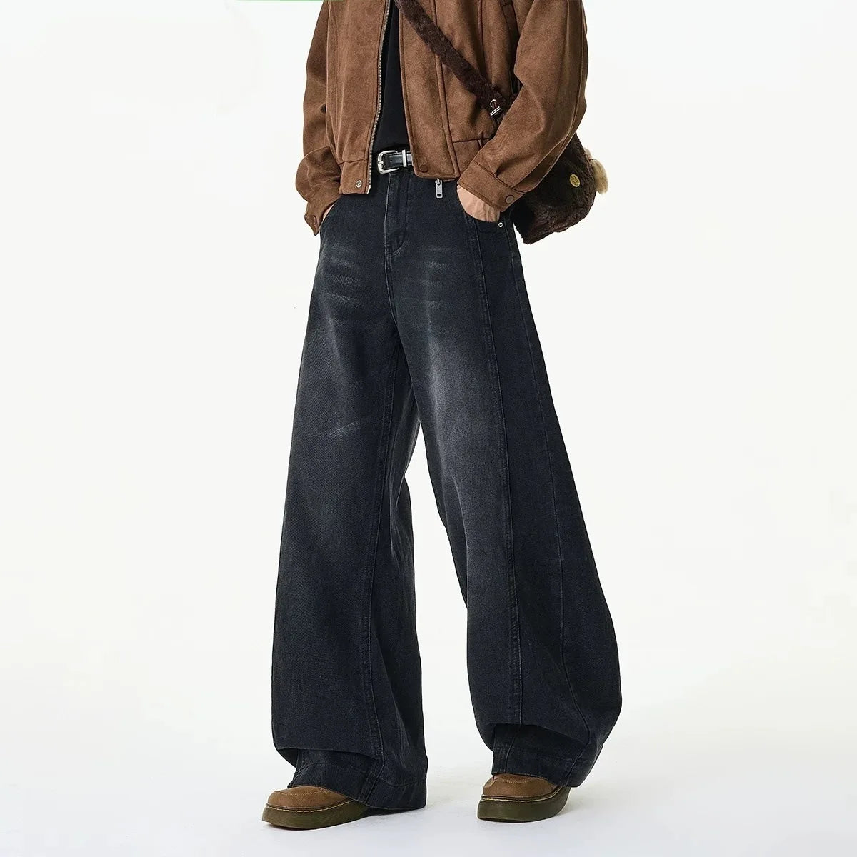 A person wearing dark wide-leg denim jeans, a brown suede jacket, and brown shoes, shown from the chest down against a plain white studio background.