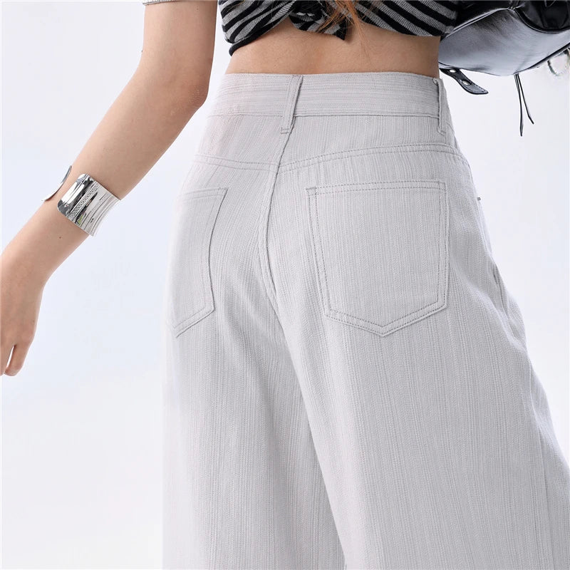 Close-up back view of a person wearing light gray wide-leg pants with two large back pockets, a black-and-white striped crop top, and a silver cuff bracelet against a plain white background.