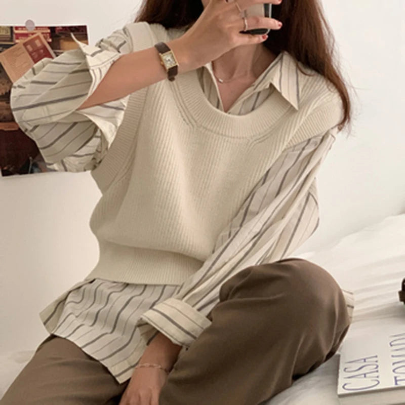 Person sitting on a couch wearing a beige sweater and striped shirt, taking a selfie.