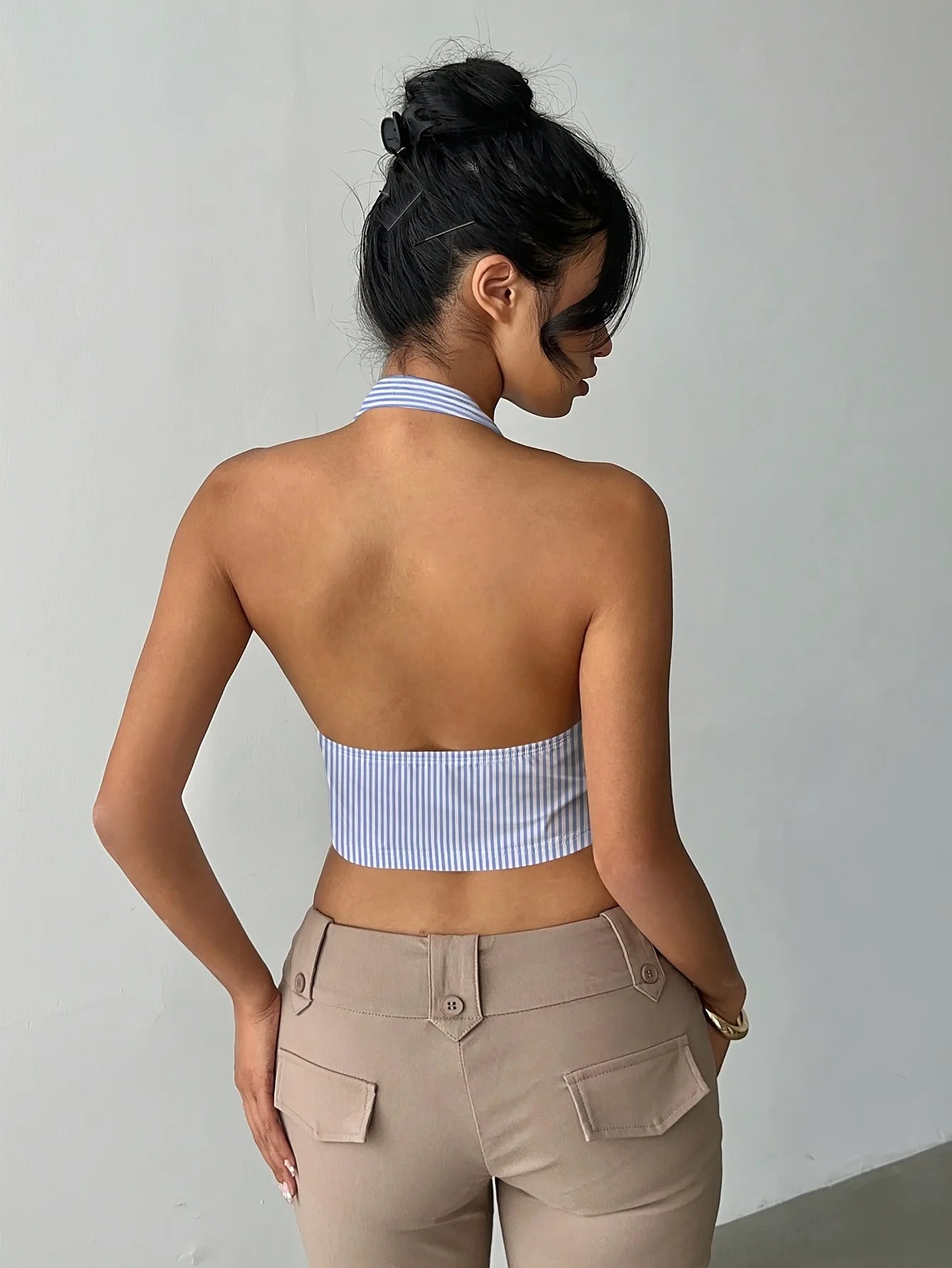 Woman wearing a striped crop top and beige pants against a plain background