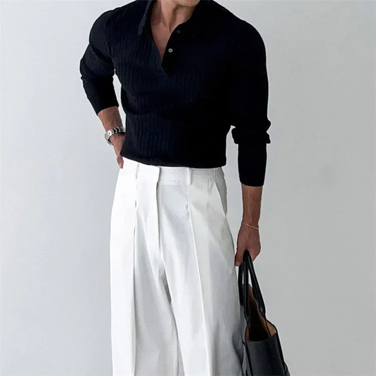 Person wearing a black sweater and white pants holding a black bag on a plain background
