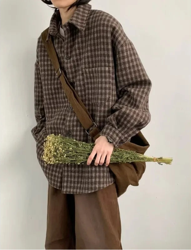 Person wearing a brown plaid shirt and holding dried flowers against a plain background