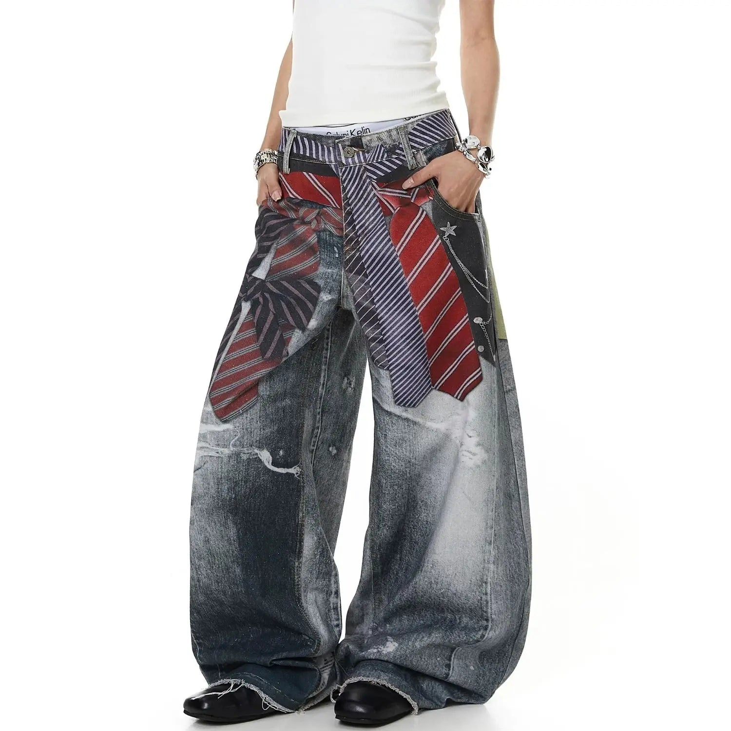 A person wearing very wide-leg distressed denim pants with a printed tie pattern, paired with a white top and black shoes, shown against a plain white background.