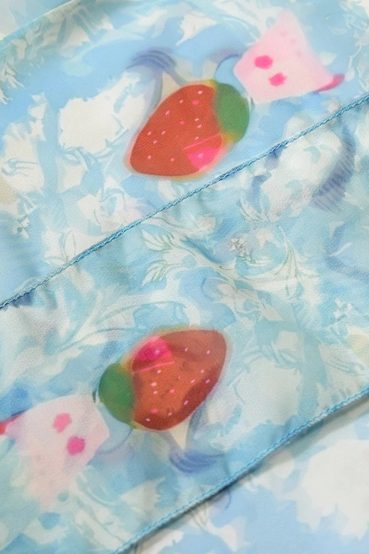 A close-up of a light blue fabric with a white floral pattern and printed strawberries, showing a diagonal stitched seam.