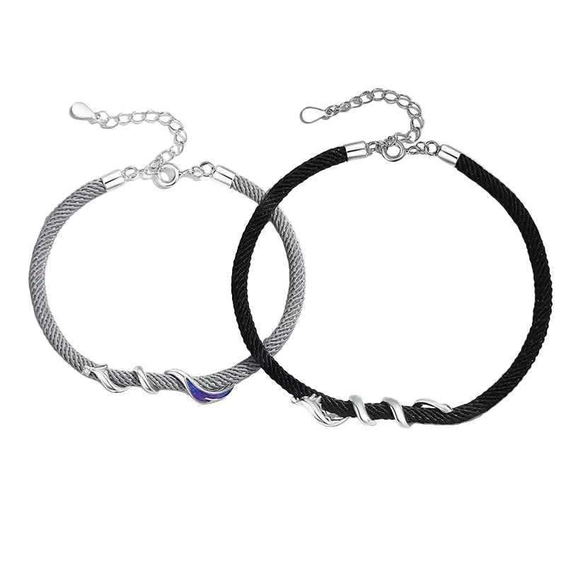 Two bracelets, one silver and one black braided, on a white surface with a blue sky background.