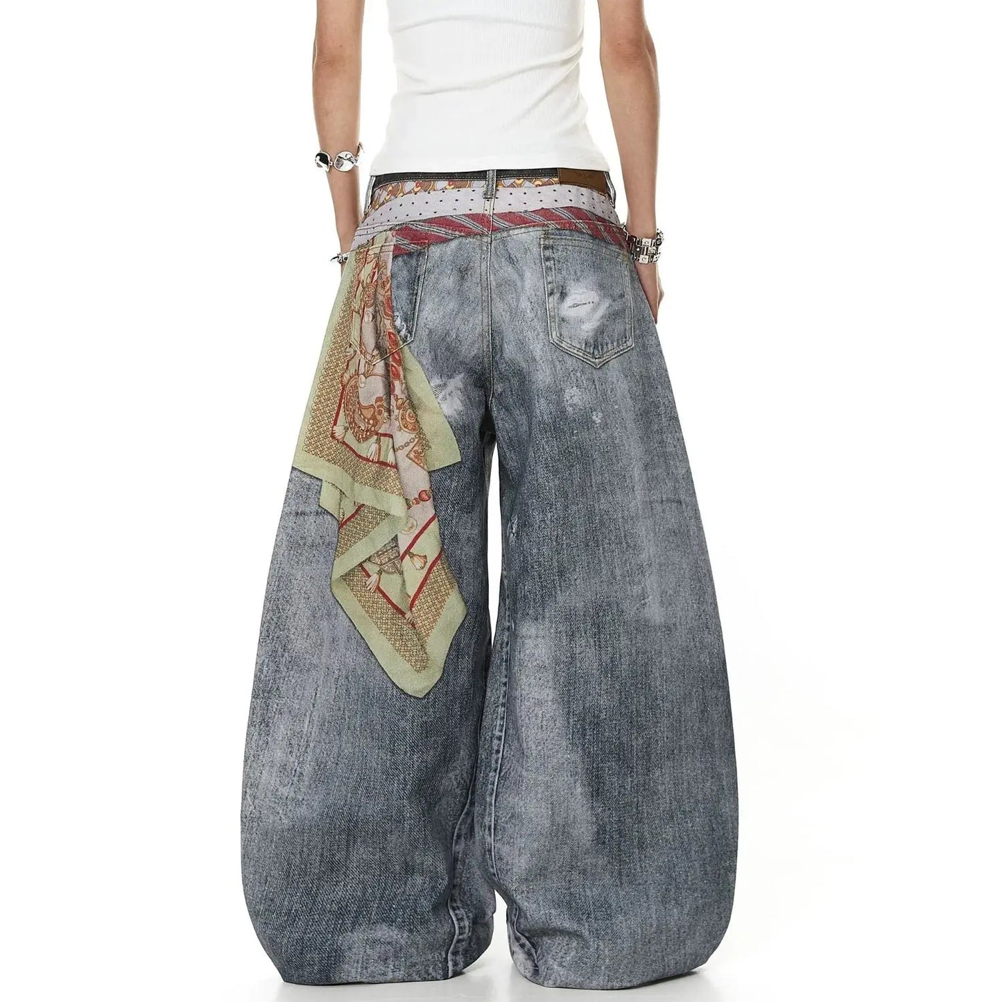 A person shown from the back wearing very wide-leg distressed denim jeans in faded blue-gray, a white top, and a patterned belt with a matching scarf tied around the back.