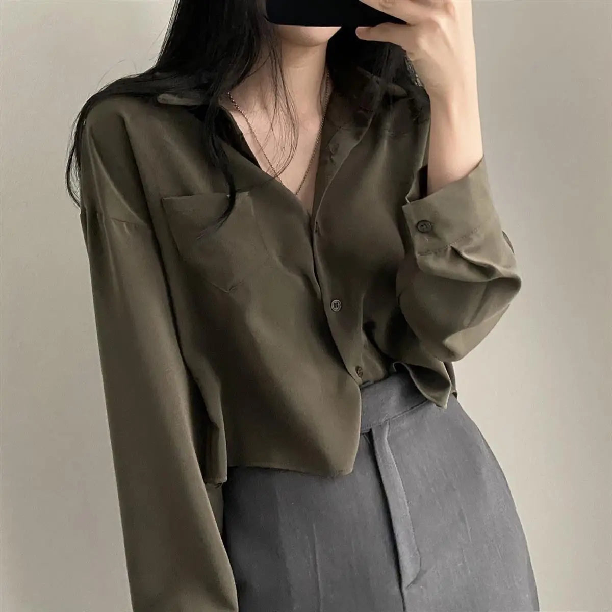 Person wearing an olive green shirt with rolled-up sleeves against a neutral background