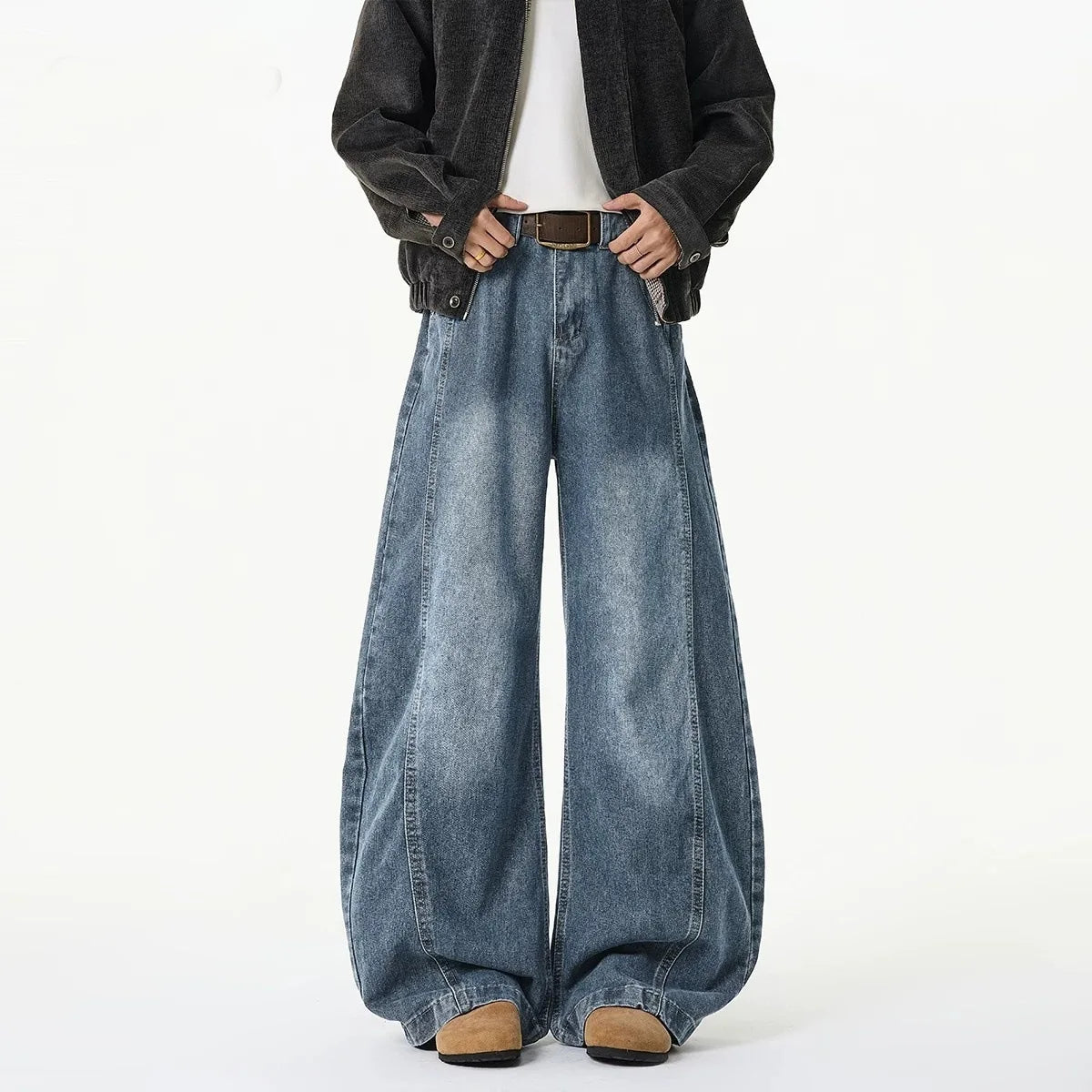 A person wearing very wide-leg blue denim jeans with a faded wash, styled with a black jacket, white shirt, and brown shoes against a plain white background.