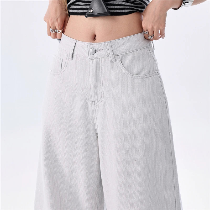 A close-up of a person wearing light gray wide-leg cropped jeans with a striped crop top, showing the waist, hands, and midriff against a plain light background.