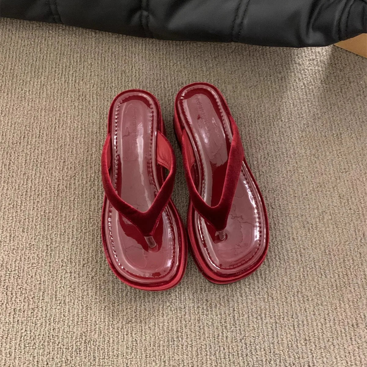 A pair of glossy red patent leather thong sandals with low block heels, shown from a top-down view on a textured beige carpet.