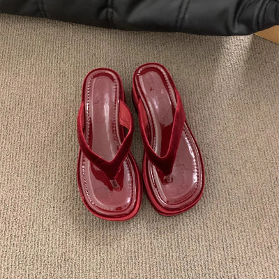 A pair of glossy red patent leather thong sandals with low block heels, shown from a top-down view on a textured beige carpet.