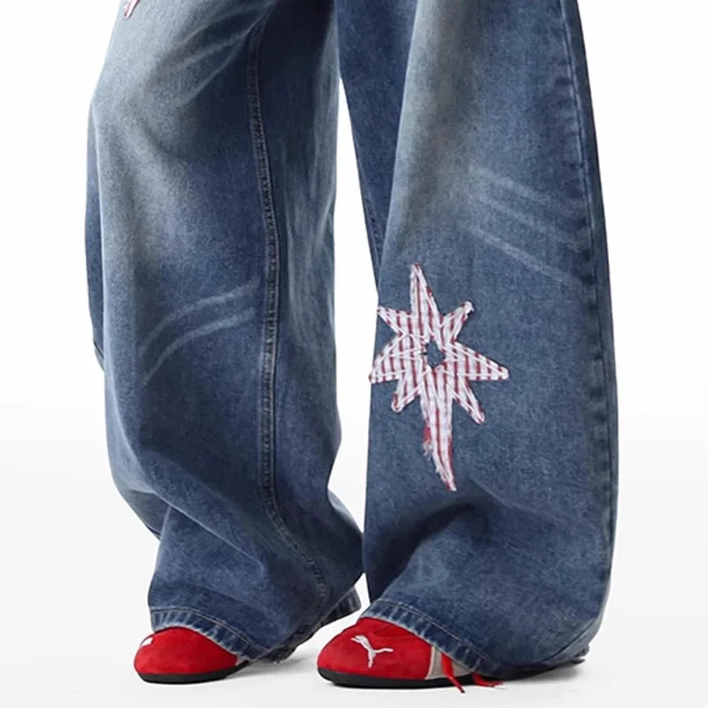 Close-up of a person's legs wearing wide-leg blue jeans with a red-and-white star patch on the left leg, paired with red slip-on shoes against a plain white background.